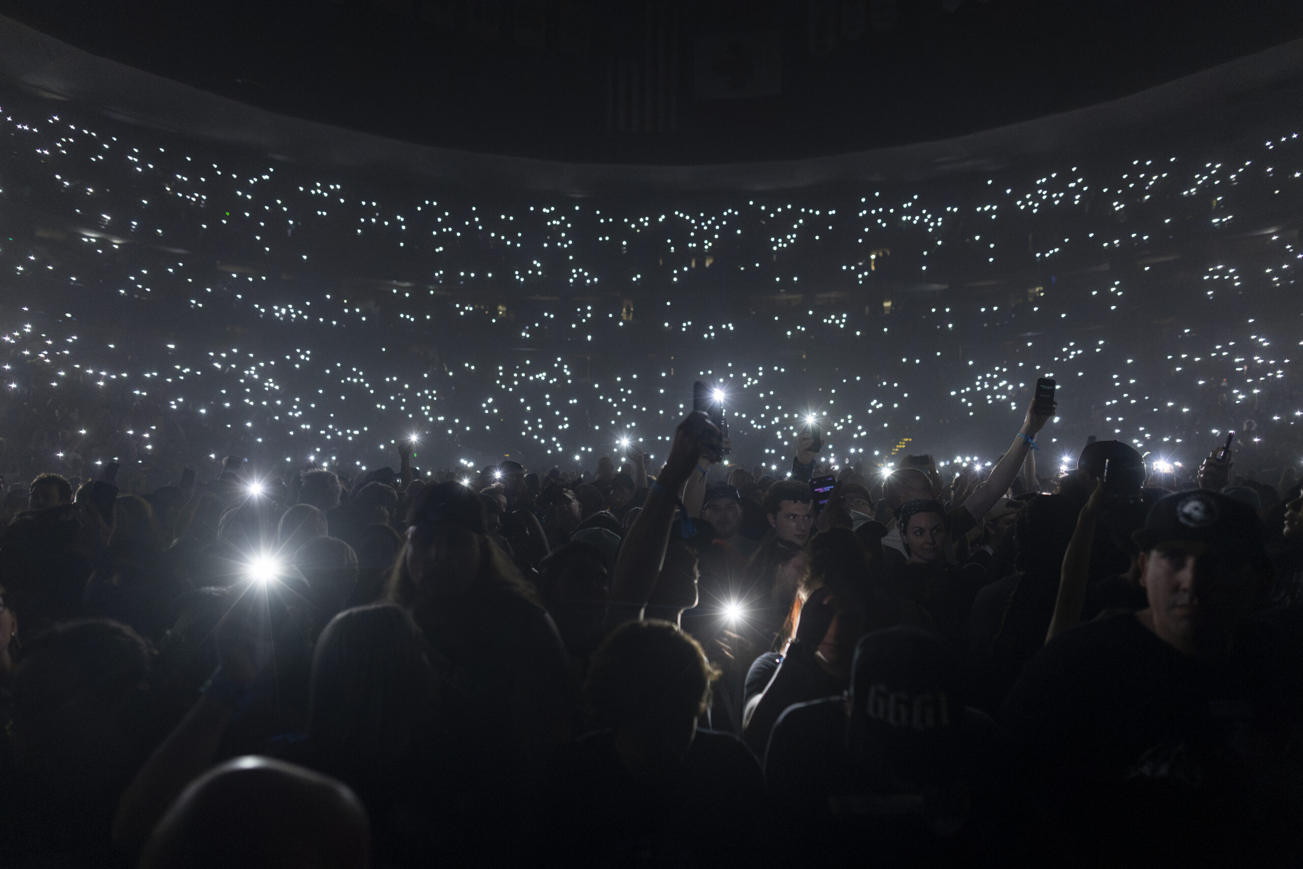 Concert crowd raises illuminated phones inside Ball Arena.