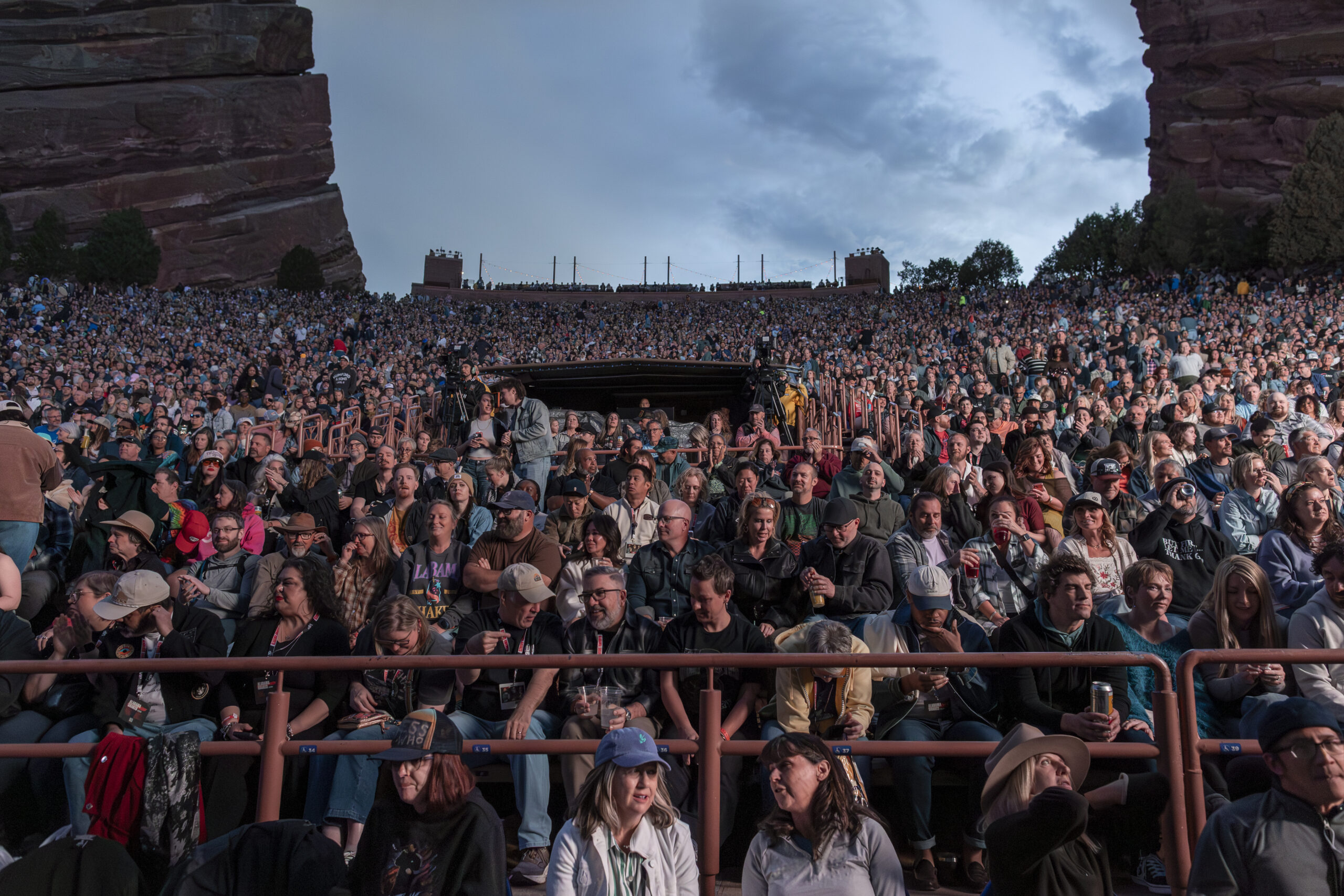 A packed Red Rocks audience waits beneath dramatic evening clouds.