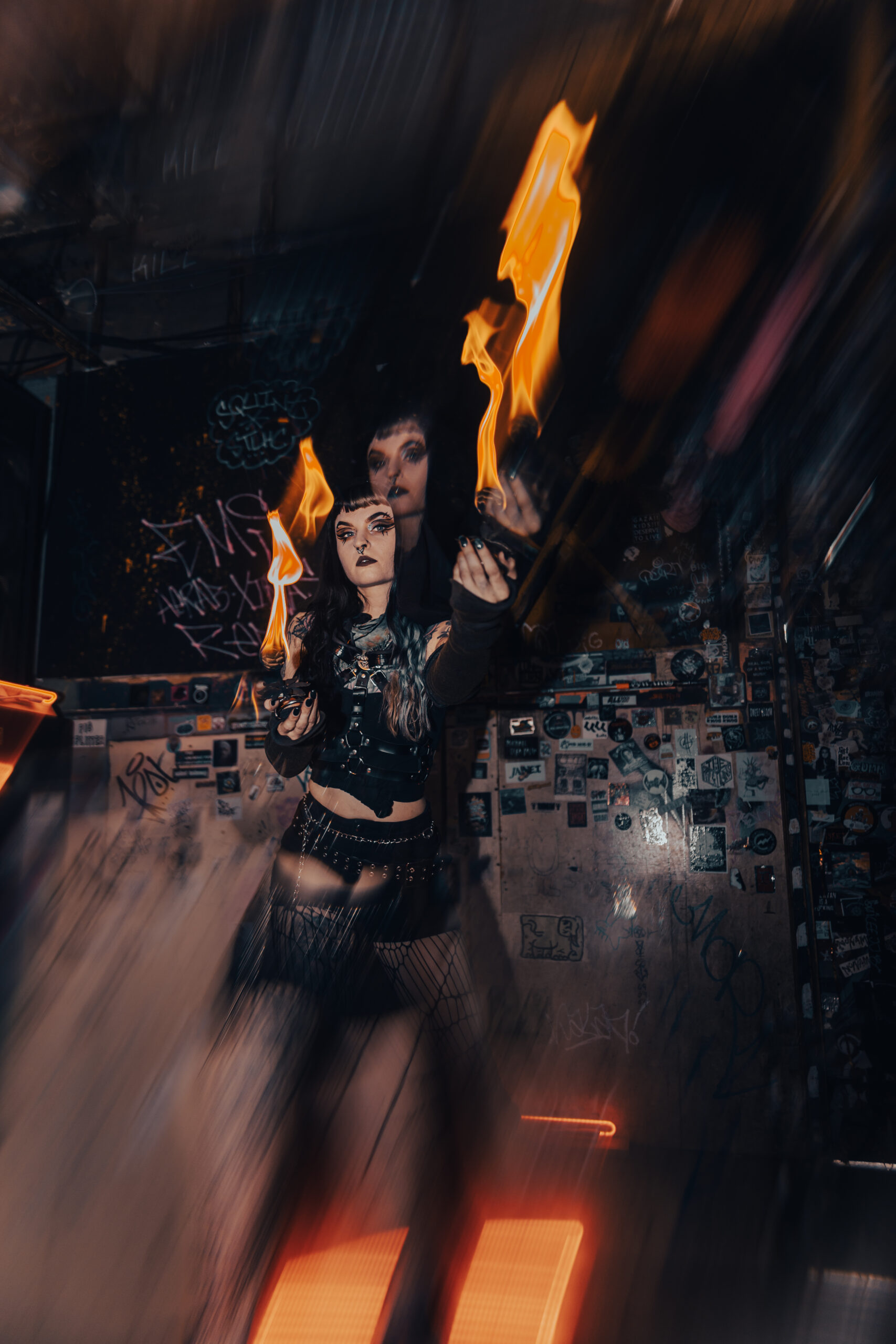 Fire performer appears through layered reflections in a dark venue.
