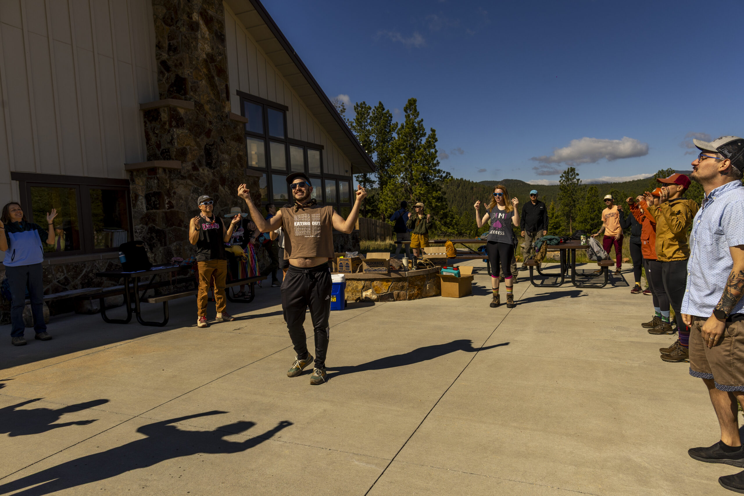 Outdoor community gathers in bright sun before a Pride hike.