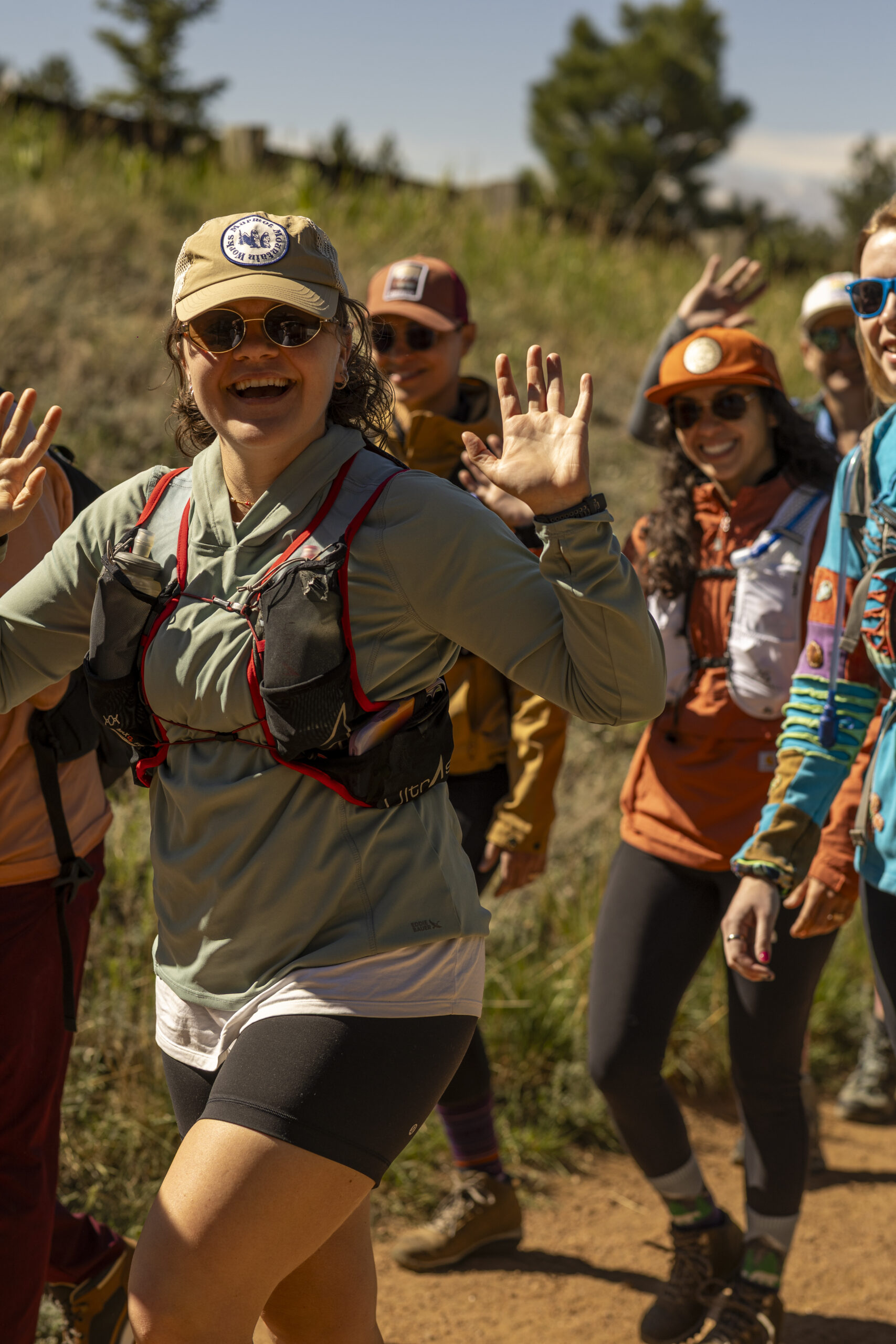 Smiling hiker waves while a colorful group gathers on the trail.