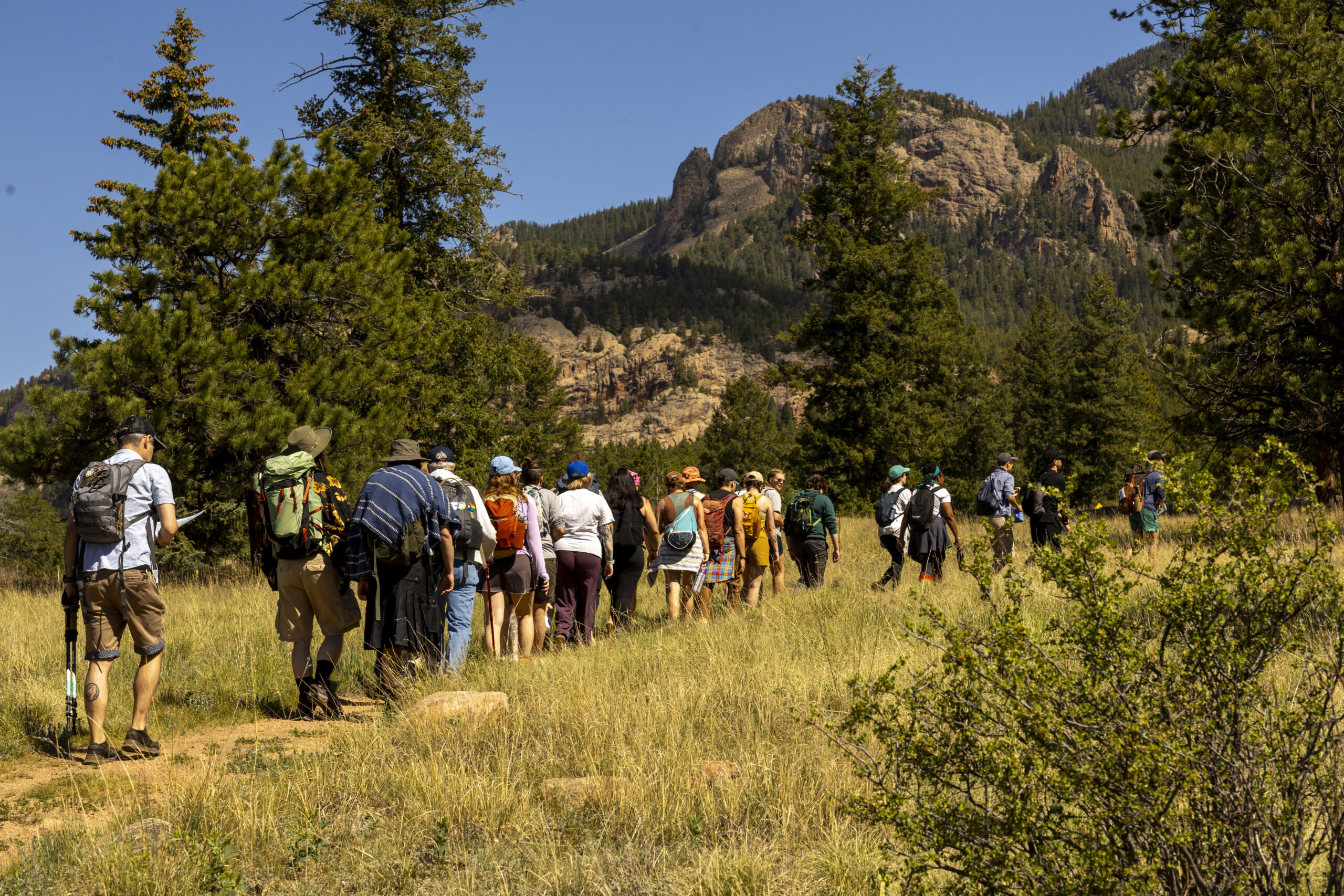 Group of hikers crosses a meadow beneath Colorado mountains.