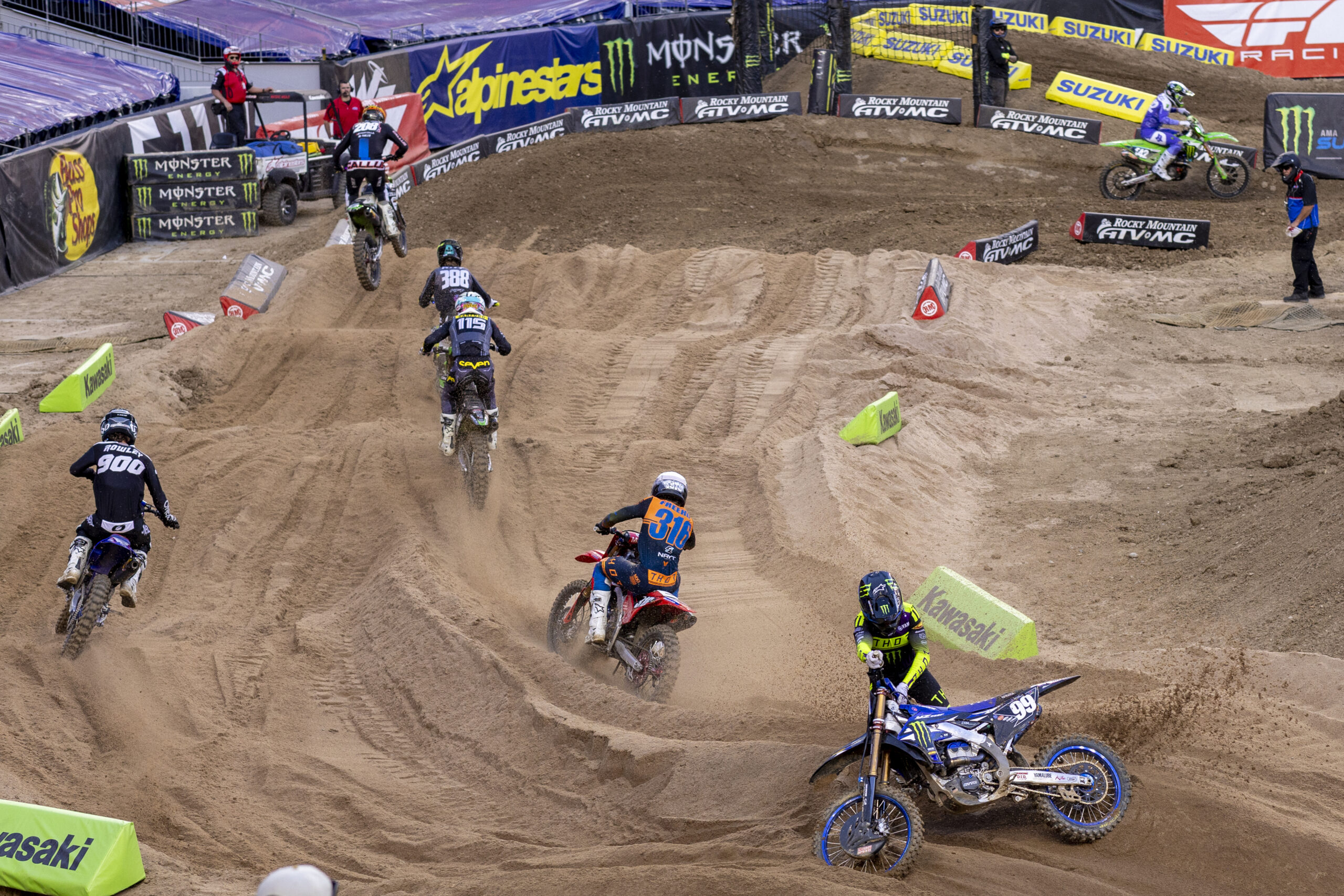 A pack of motocross riders charges across the SMX dirt course.