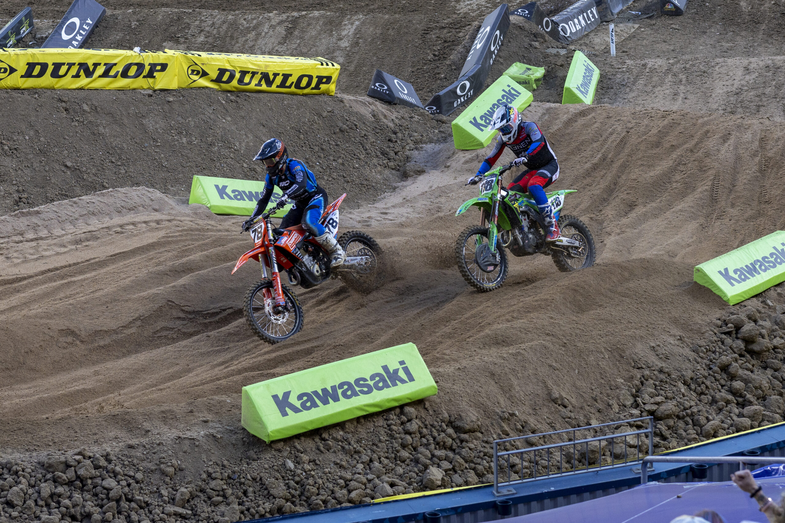 Two riders race through a dirt turn during SMX Supercross.