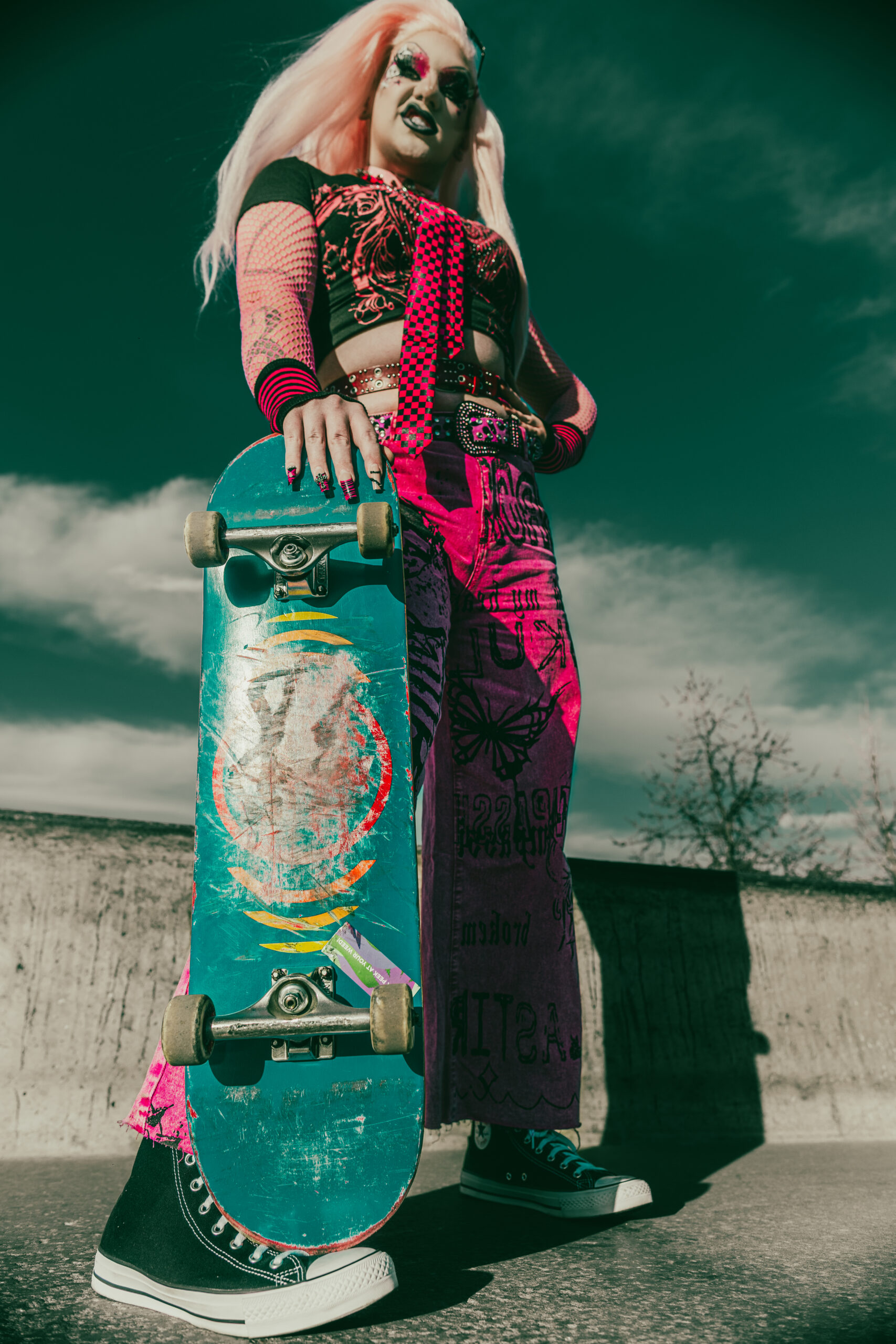 Minerva poses with a skateboard beneath a dramatic sky.