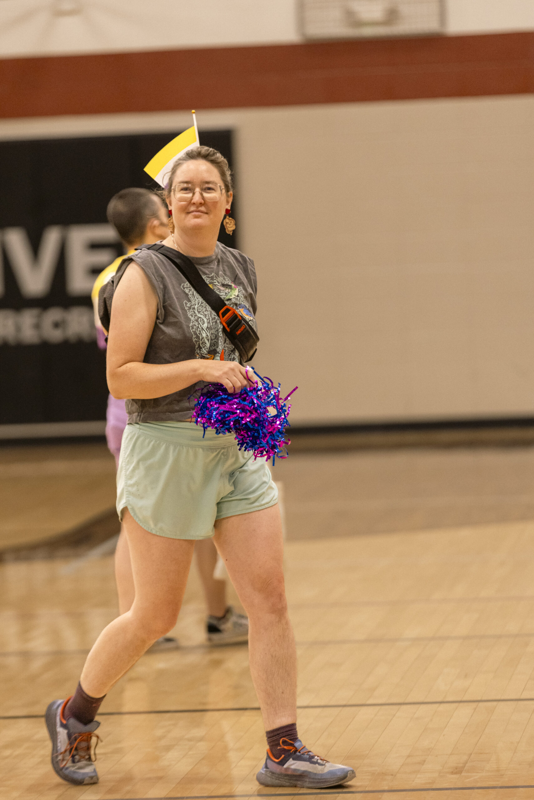 Supporter carries colorful pom-poms beside a community basketball court.