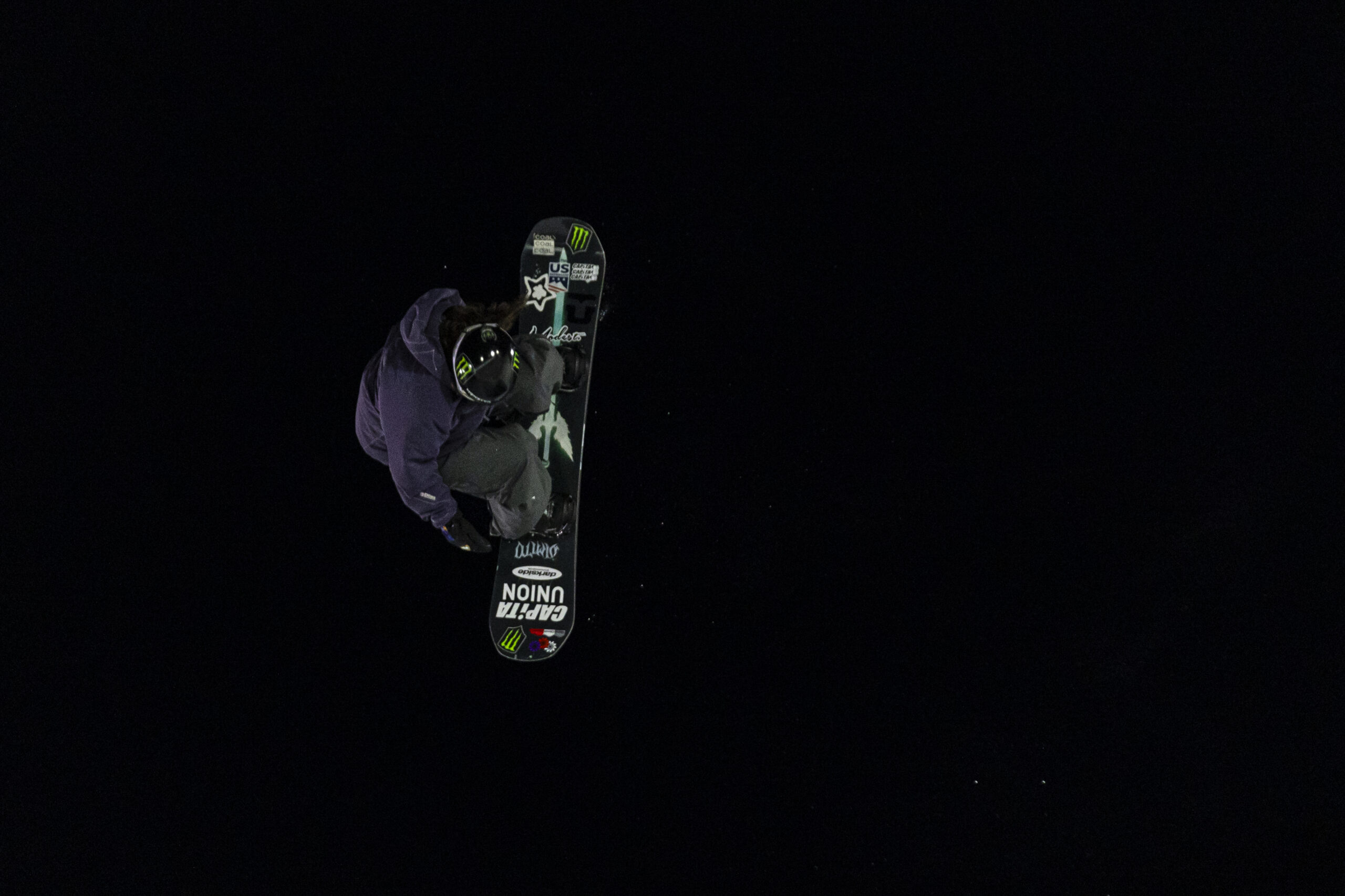 Snowboarder tucks into an aerial trick against the night sky.